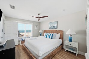 A bedroom with a bed, a ceiling fan, a window with a view, a bedside table with a lamp, and a painting on the wall. - Beach Front Home, Sleeps 9 (Cape San Blas)