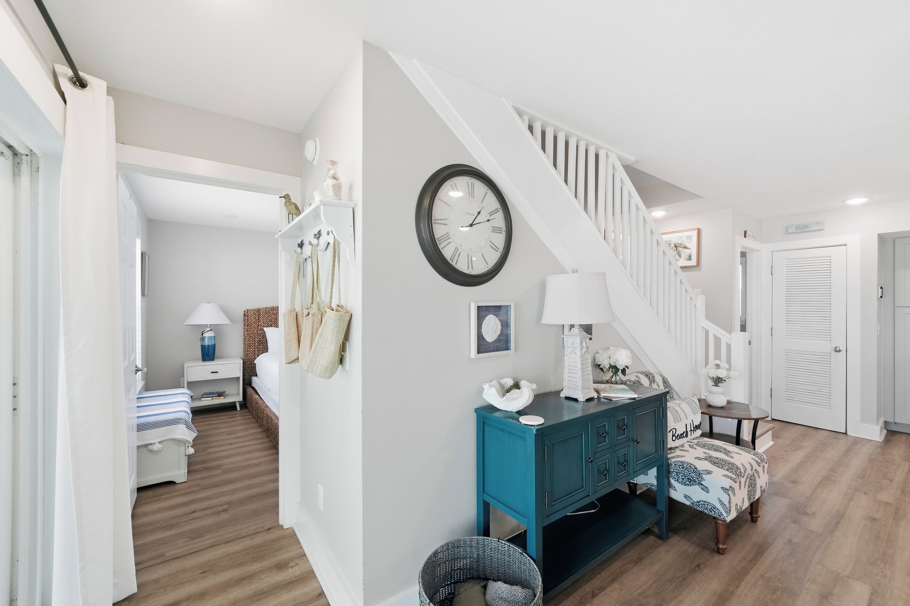A modern interior with a staircase, a clock, and a teal-colored cabinet.