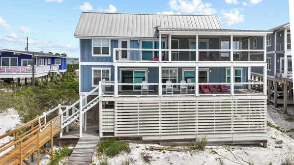 Ein mehrstöckiges Gebäude direkt am Strand mit einer Holzterrasse und Treppen zum Eingang.