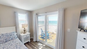 A bedroom with a bed, nightstand, lamp, and a TV. There is a balcony with a chair and a view of the beach. - Pet Friendly Beach Front Home (Cape San Blas)