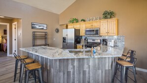 A modern kitchen with a central island, wooden cabinets, stainless steel appliances, and a bar stool seating area. - Moab Basecamp! 10 min to Arches | Pool & Hot tub (Moab)