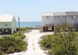 Un chemin menant à une propriété située en bord de mer, comprenant deux bâtiments : l’un, surélevé sur des piliers, et l’autre, reposant sur une fondation surélevée, le tout entouré de végétation.