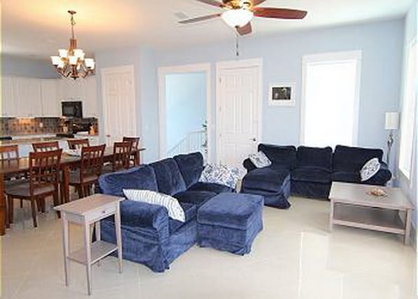 A living room with a blue sectional sofa, a dining area with wooden chairs, and a kitchen in the background. - 1st Tier Home with Private Pool! (Cape San Blas)