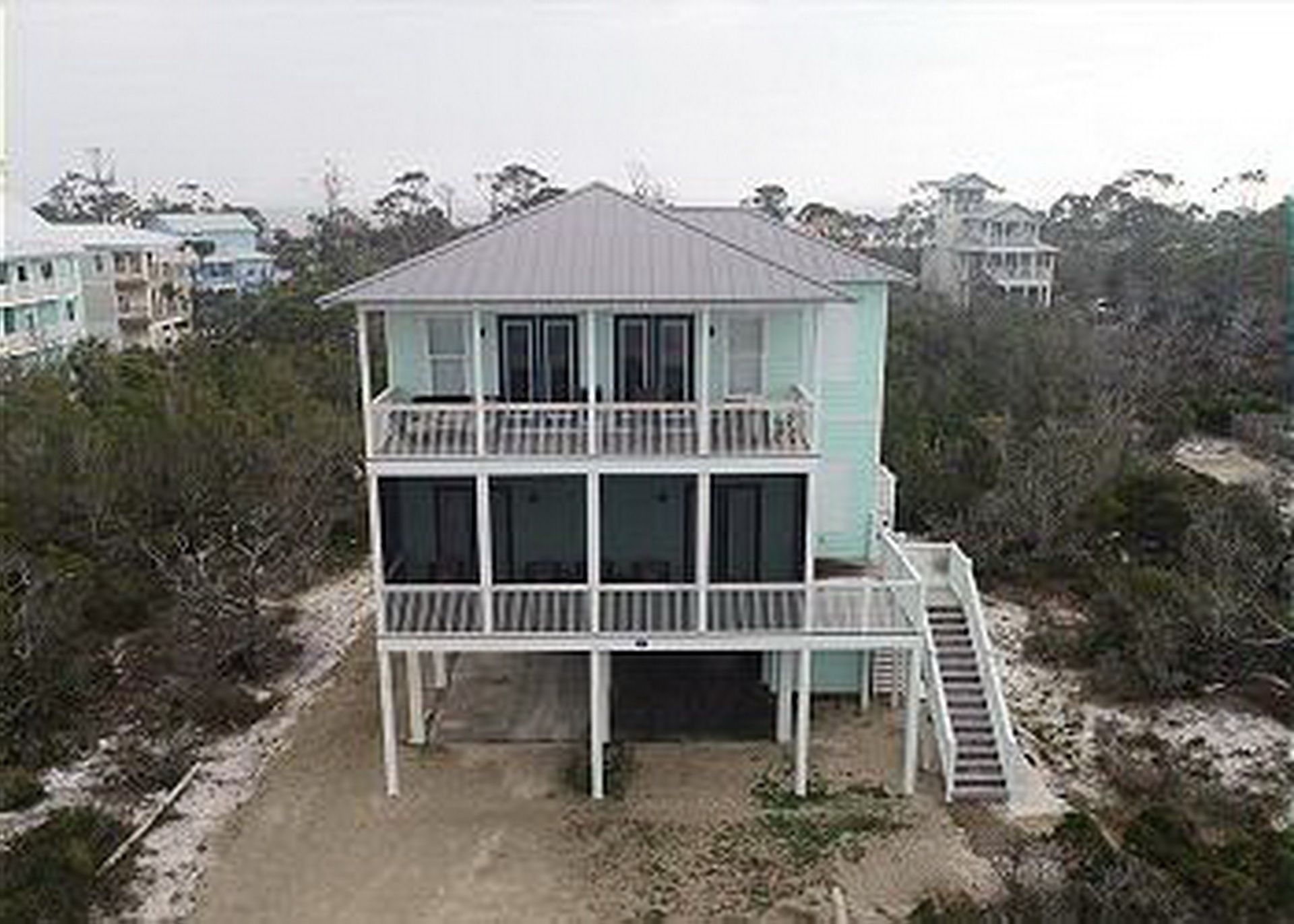 Ein zweigeschossiges Strandhaus mit einem Balkon im oberen Geschoss und einer Treppe zum Haupteingang.