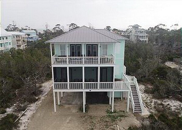 A two-story beachfront house with a balcony on the upper floor and a staircase leading to the main entrance.