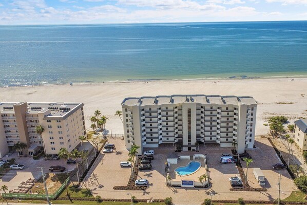A beachfront hotel with multiple buildings, a swimming pool, and a parking area.
