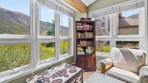 Quarto com grandes janelas com vista para as montanhas, uma estante de livros e uma poltrona de couro.