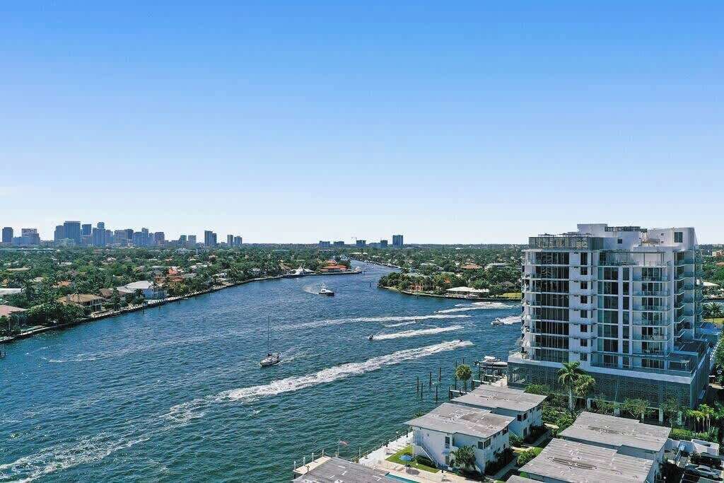 Un hotel moderno con vista a un río con barcos, rodeado de vegetación y otros edificios.