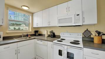 A modern kitchen with white cabinets, a built-in microwave, a stove, and a window with a view of buildings.