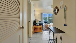 Un couloir avec une porte, un canapé, une table basse, une lampe et une table à manger.