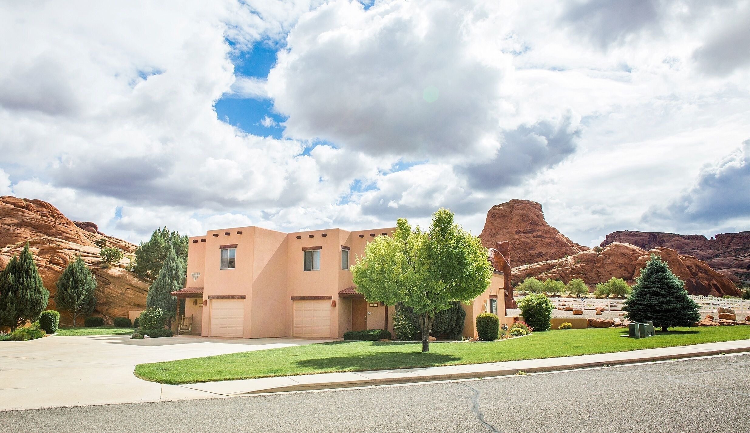 A modern building with a flat roof and a garage, surrounded by a well-maintained lawn and trees, with red rock formations in the background.