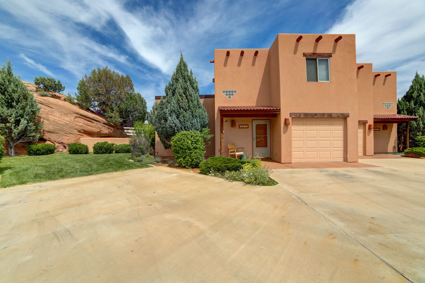 A single-story house with a garage, surrounded by a well-maintained lawn and a large rock formation.