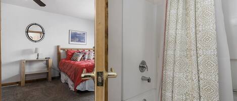 Un dormitorio con cama, mesita de noche, ventilador de techo, espejo montado en la pared y un cuadro enmarcado.