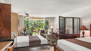A hotel room with a bed, a desk, a chair, a table, and a view of a garden.