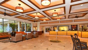 A spacious lobby with a reception desk, seating area with sofas and chairs, and a decorative ceiling with recessed lighting.