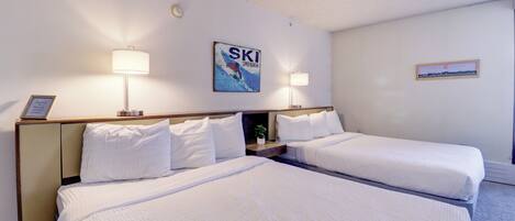 A hotel room with two beds, a ski-themed wall art, and a framed certificate on the left side.