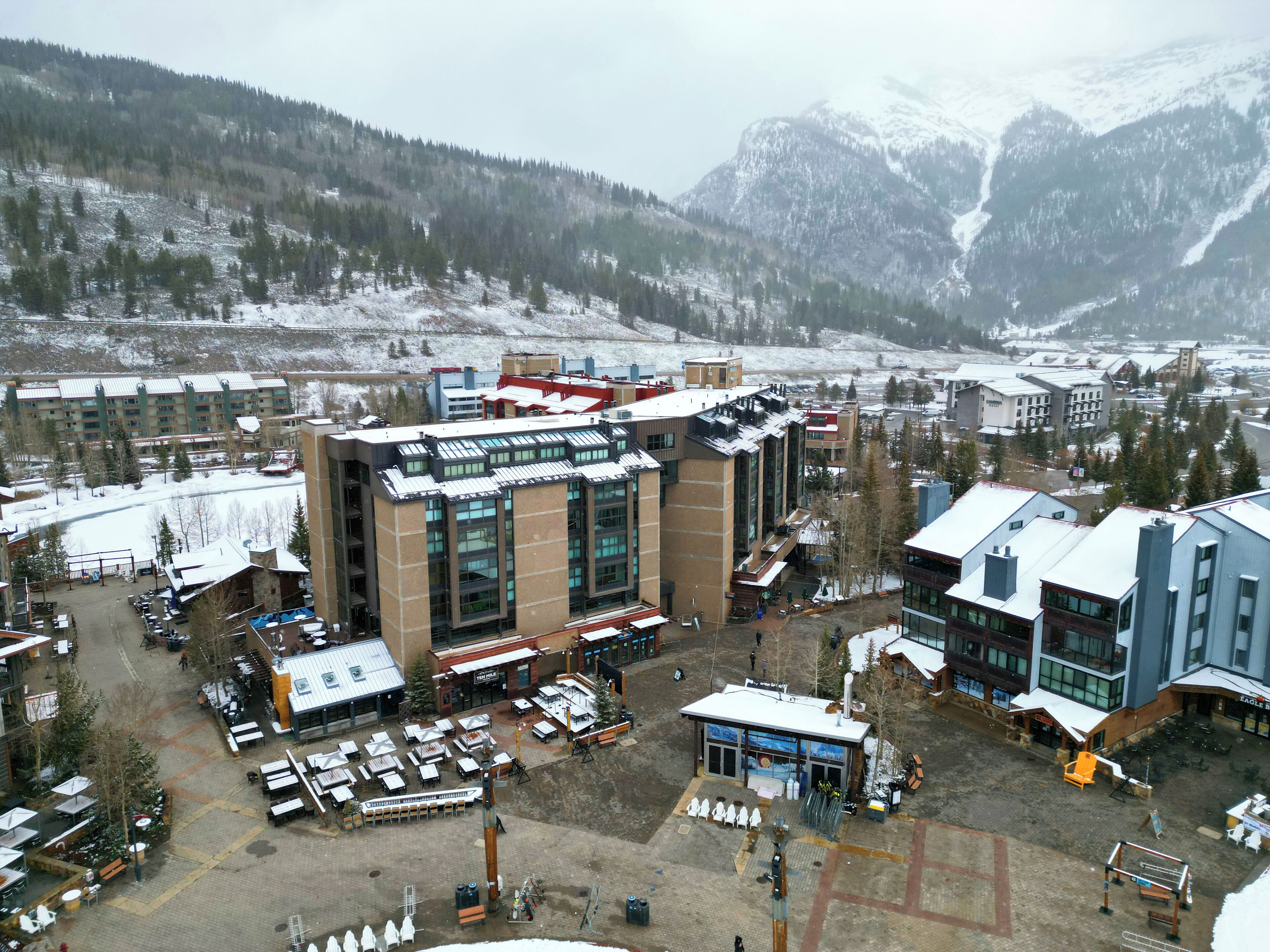 Un hotel moderno con un edificio principal, rodeado de un estacionamiento y un paisaje montañoso.