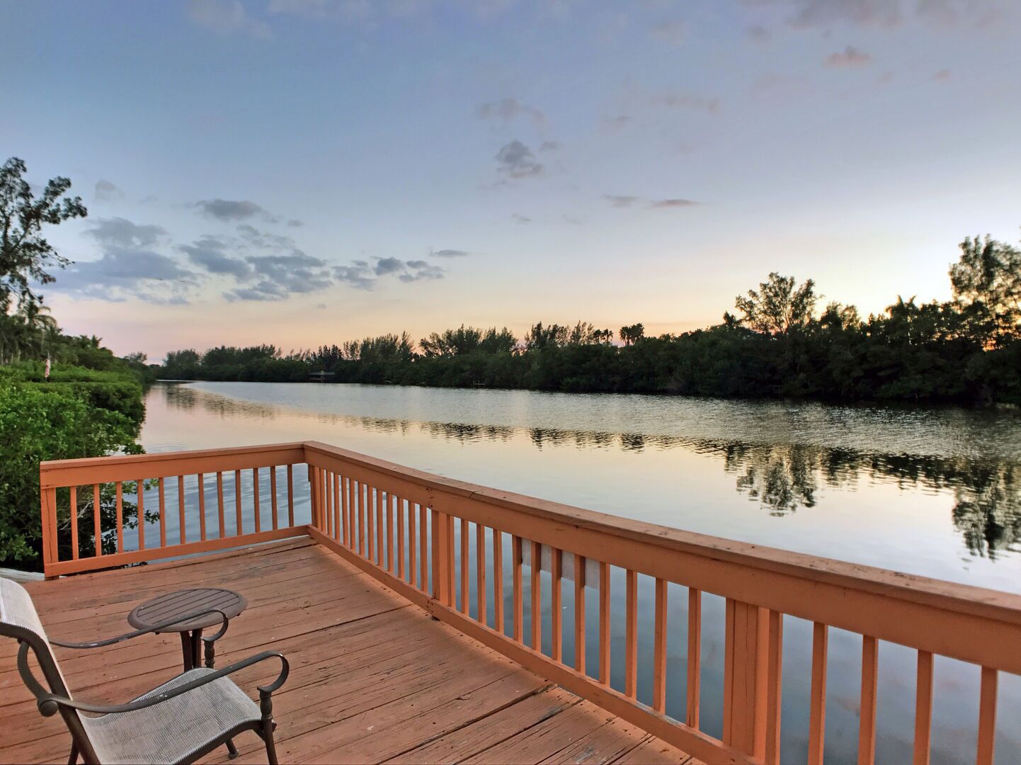 A wooden deck with a railing overlooking a calm river, surrounded by trees.