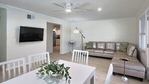 A modern living room with a flat-screen TV, a dining table with chairs, a sofa, and a ceiling fan. - Small and Quiet Lakefront Resort on Siesta Key W/ Heated Pool and Kayaks (Siesta Key)