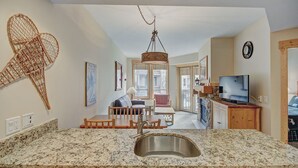 Una cucina con piani di lavoro in granito, lavello in acciaio inossidabile, mobili in legno, un lampadario e un'area pranzo con tavolo e sedie.