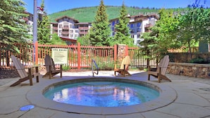 Area piscina con poltrone Adirondack, un cartello con le regole della spa e vista su montagne e edifici sullo sfondo.