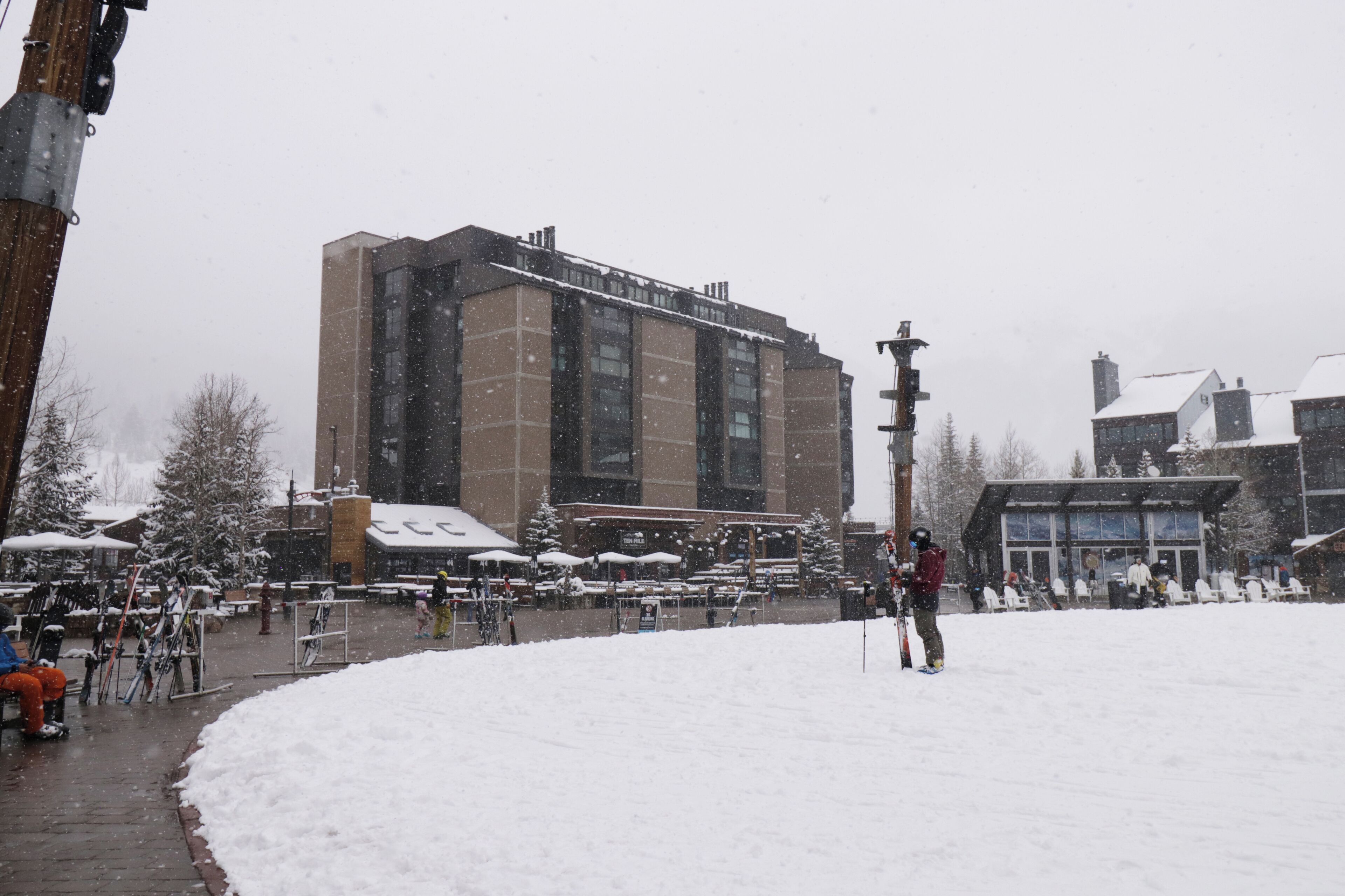Zona esterna innevata con un edificio sullo sfondo, panchine e persone.