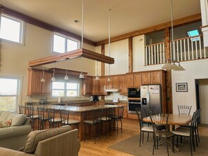 A spacious kitchen with wooden cabinets, a central island with bar stools, a dining table with chairs, and a view of the upper floor. - 6 bdrm home W/Beach & Bay Access (Cape San Blas)