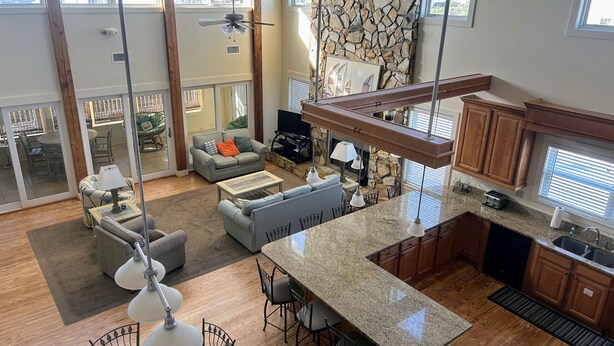 A spacious living area with a large sofa, a coffee table, and a dining area with chairs. There is a kitchen with granite countertops and wooden cabinets.