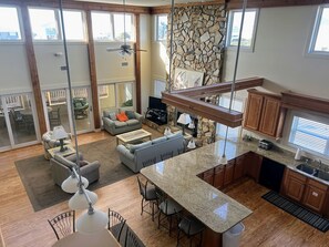 A spacious living area with a large sofa, a coffee table, and a dining area with chairs. There is a kitchen with granite countertops and wooden cabinets.