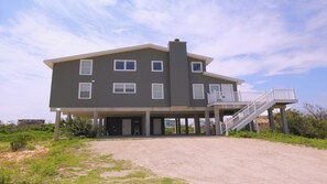 A two-story building with a balcony and a staircase leading to it, surrounded by a gravel driveway and greenery. - 6 bdrm home W/Beach & Bay Access (Cape San Blas)