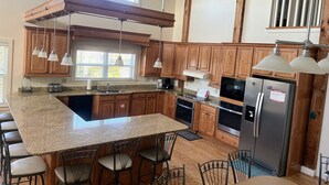 A kitchen with wooden cabinets, granite countertops, a central island with bar stools, stainless steel appliances, and pendant lighting.