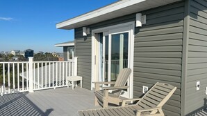 A deck with two lounge chairs and a small table, a white railing, and a building with grey siding.