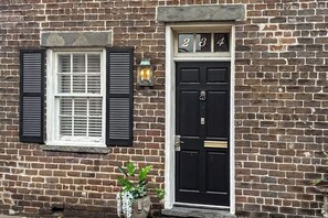 A brick building with a black door, a window with shutters, and a potted plant.