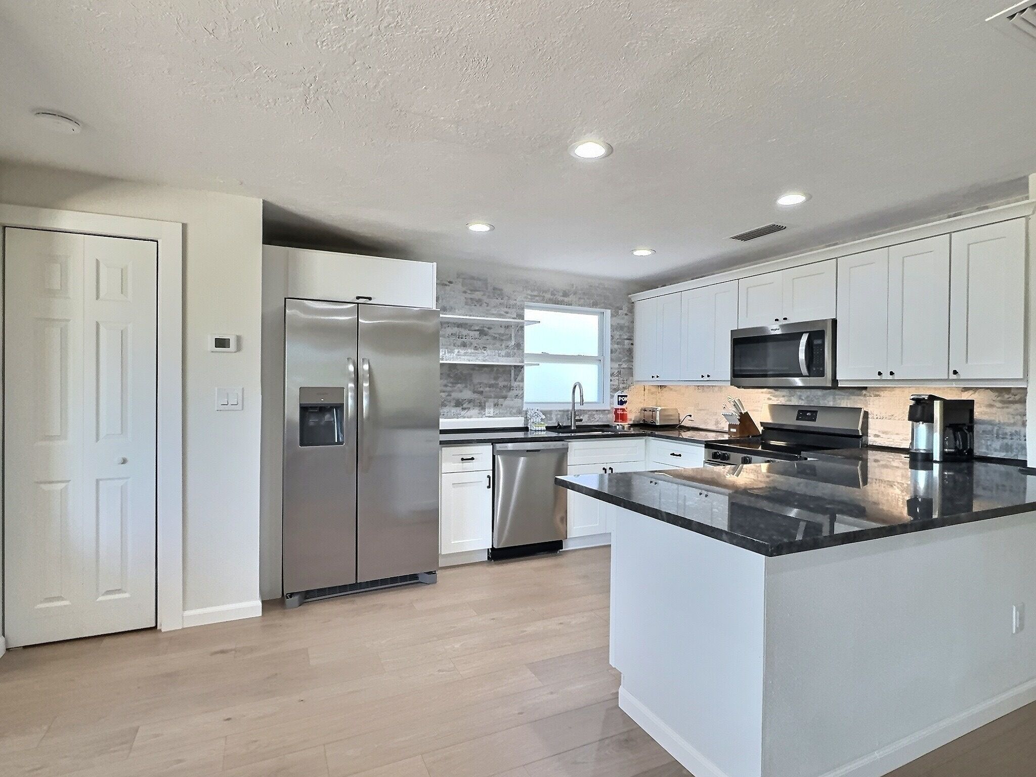 A modern kitchen with white cabinets, stainless steel appliances, and a large island.