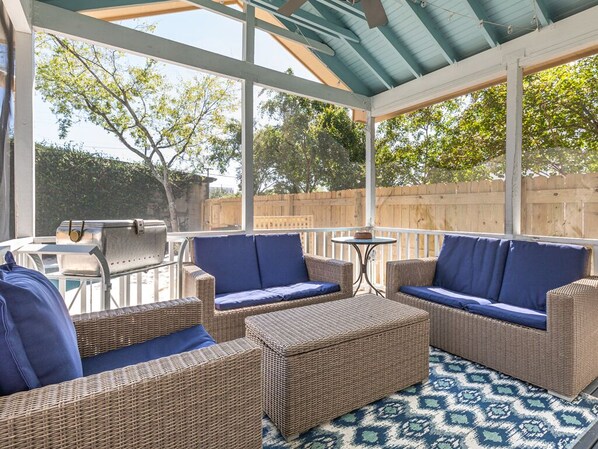 A covered outdoor patio with wicker furniture and a grill.
