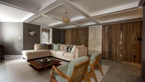 Ein Wohnzimmer mit einem Ecksofa, zwei Sesseln, einem Couchtisch und einer Wand als Holzdekor.