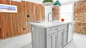 Eine Küche mit weißer Arbeitsplatte, grauen Schränken und einer Holzwand.