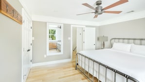 A bedroom with a bed, a ceiling fan, a wooden floor, and a view of a balcony.