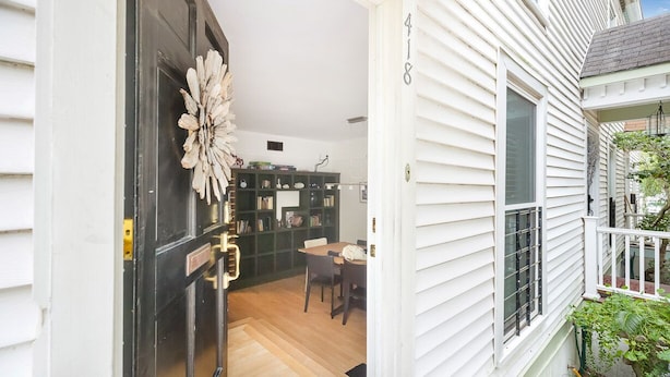 A white house with a black door, a dining area with a table and chairs, and a green bookshelf.