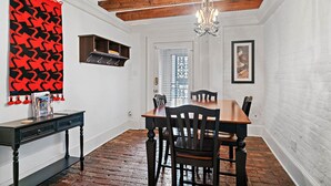 Un coin repas avec une table en bois, des chaises, un lustre et un rideau rouge à motifs.