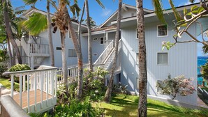 A beachfront hotel with multiple-story buildings, a wooden deck, and lush tropical vegetation. - Poipu Palms #201 By Parrish Kauai- oceanfront views & see turtles! (Koloa)
