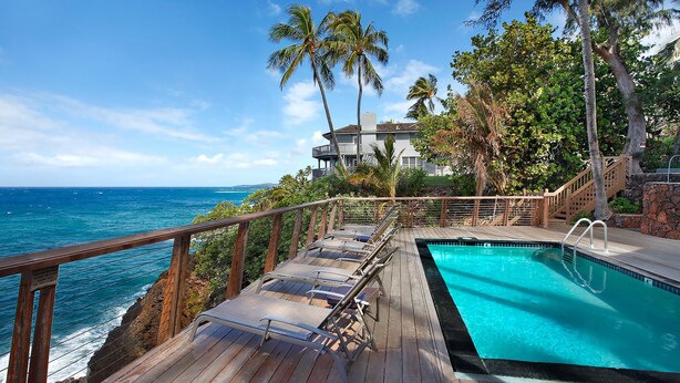 A wooden deck with a pool, overlooking the ocean with palm trees and a building in the background. - Poipu Palms #201 By Parrish Kauai- oceanfront views & see turtles! (Koloa)