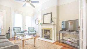 A living room with a fireplace, a television, and two patterned armchairs. - Well Appointed Row Home w/ King, Across from Forsyth Park by Lucky Savannah (Savannah)