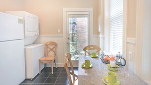 A compact kitchen with white cabinetry, two wooden chairs, a granite countertop, and a door leading to a balcony with a view of a brick wall. - Well Appointed Row Home w/ King, Across from Forsyth Park by Lucky Savannah (Savannah)
