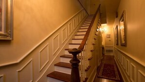 Eine Treppe mit hölzernem Geländer und weißen Spindeln, die zu einer Empfangsebene mit rotem Teppich führt.
