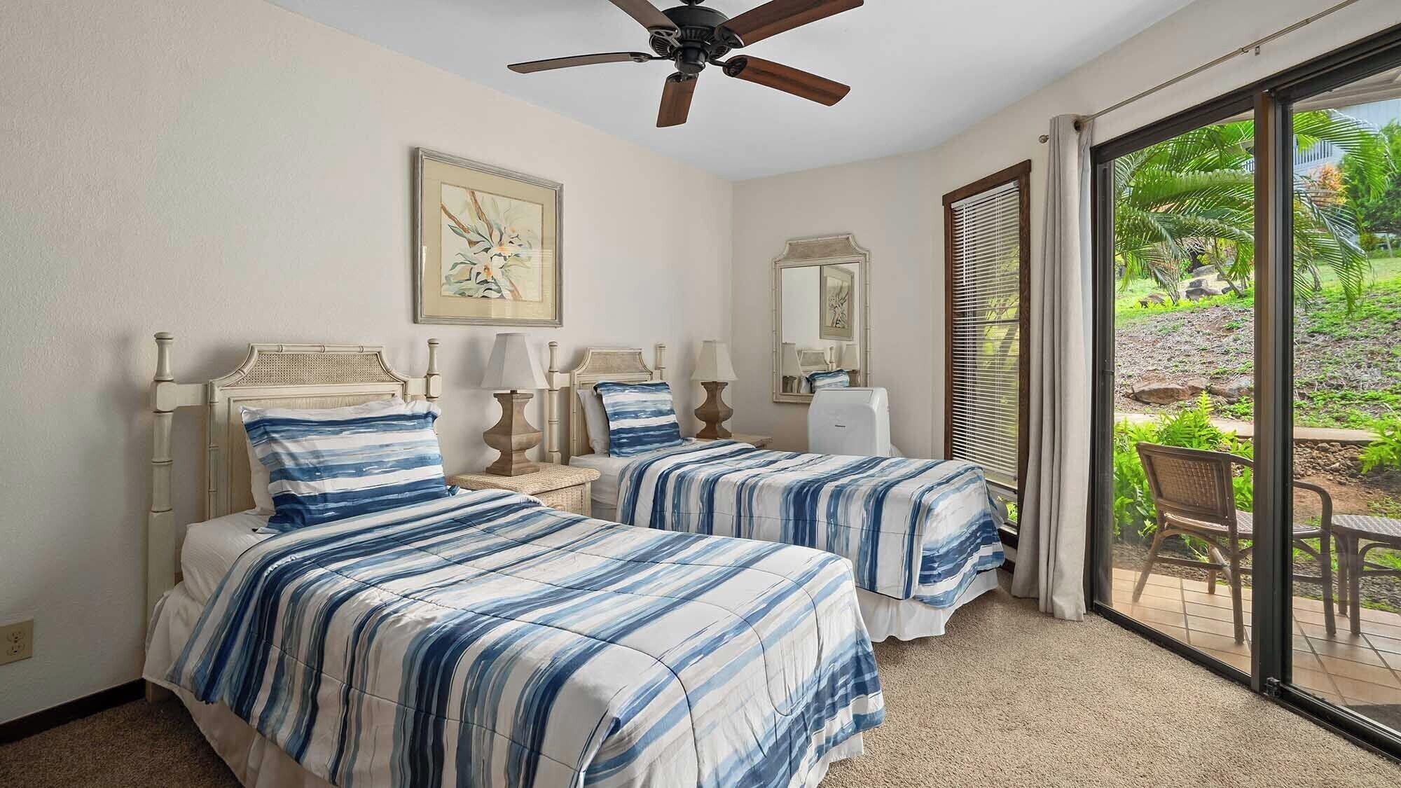 A bedroom with two beds, a ceiling fan, and a large sliding glass door leading to a garden.
