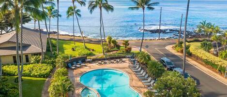 A resort with a swimming pool, lounge chairs, and a view of the ocean.