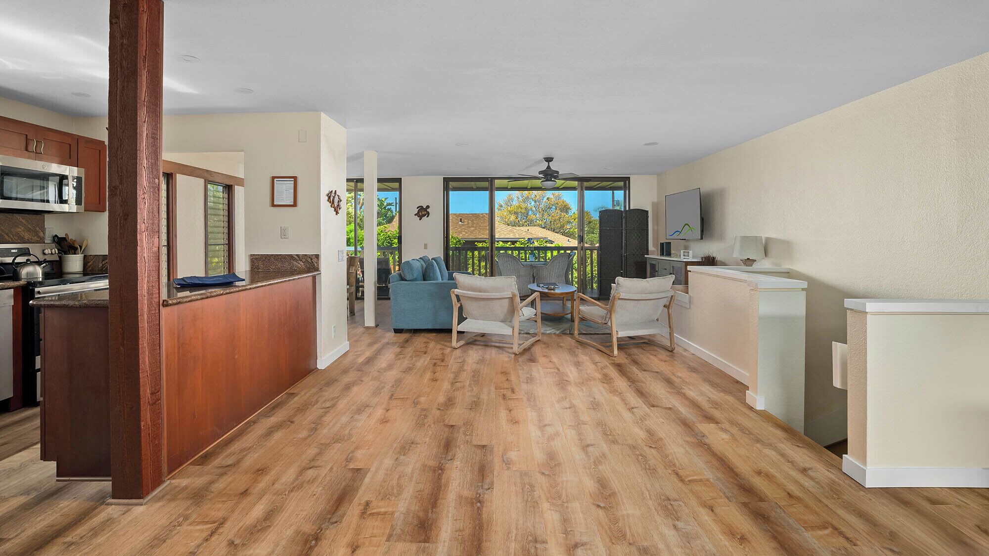 Uma sala de estar ampla com piso de madeira, cozinha equipada com micro-ondas e uma área de estar com um sofá azul e duas poltronas.