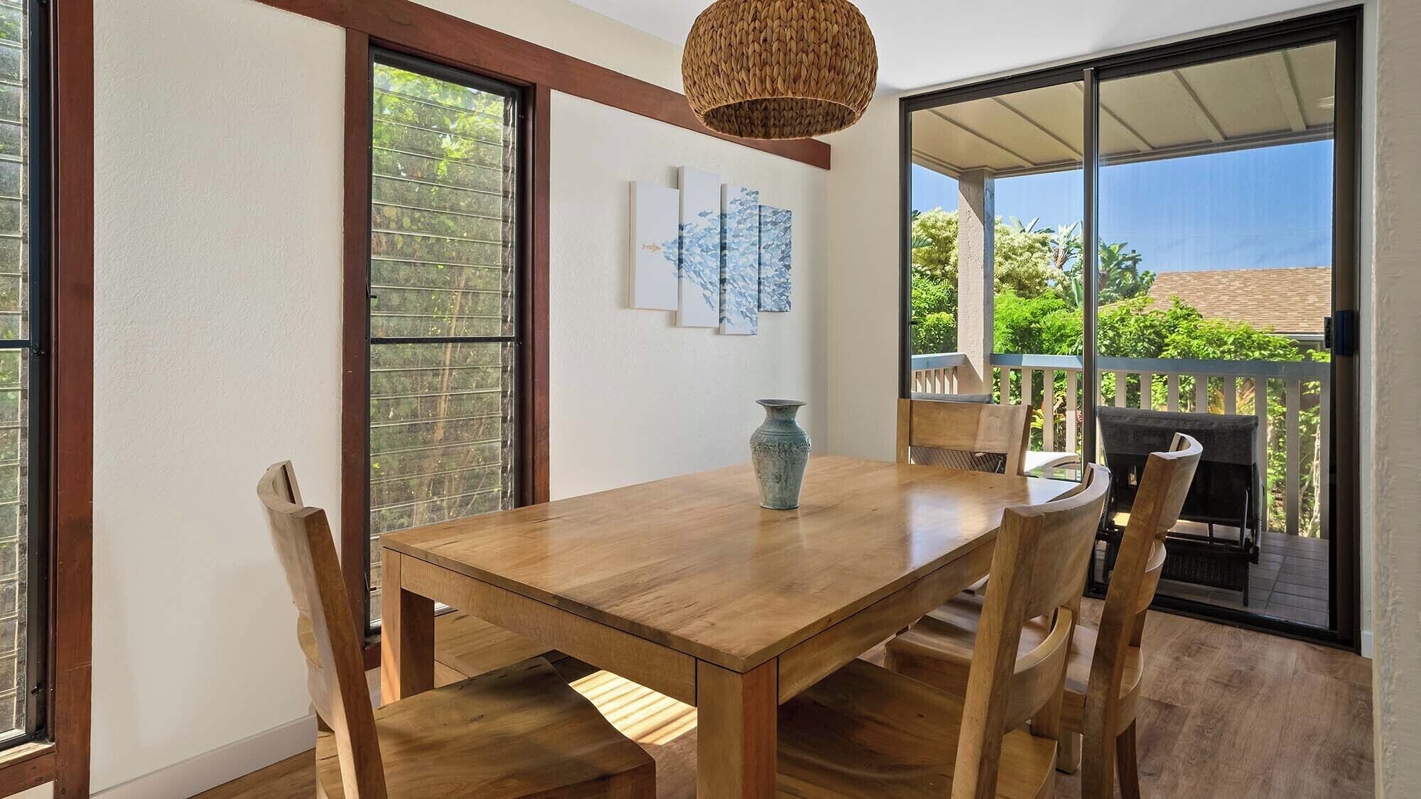Un comedor con una mesa y sillas de madera, un jarrón y vistas a un balcón con mobiliario exterior.