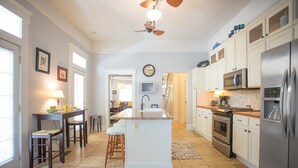 Un'ampia cucina con isola centrale, mobili bianchi, elettrodomestici in acciaio inossidabile e una ventola a soffitto.